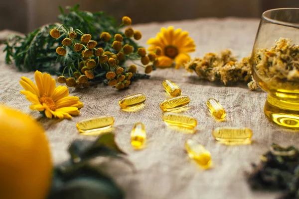 Balık yağı kapsülleri, tansi, kuru papatya çiçekleri, limon, takvim, cam bardak, ahududu yaprağı masadaki keten kumaş üzerinde, boşluğu kopyala