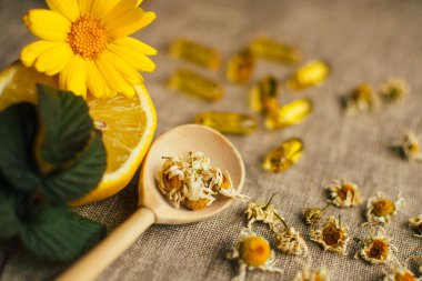 Kuru papatya çiçekli ahşap kaşık, limon, takviye, ahududu yaprağı ve masadaki keten kumaşın üzerindeki bulanık balık yağı kapsülü, boşluğu kopyala