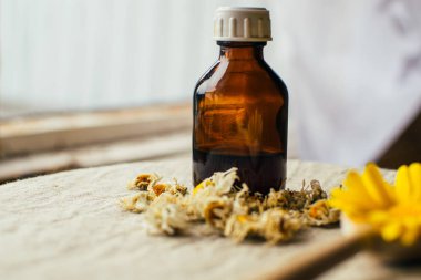 Eczane şişesindeki bitkisel tentür, papatya çiçekleri ve ahşap kaşıkta sarı sarı çiçek keten tekstil, alternatif tıp.