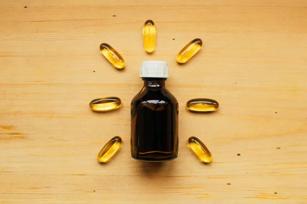 药瓶中的草药药水和木桌传统医学概念中射线形状的黄鱼油胶囊 — 图库照片