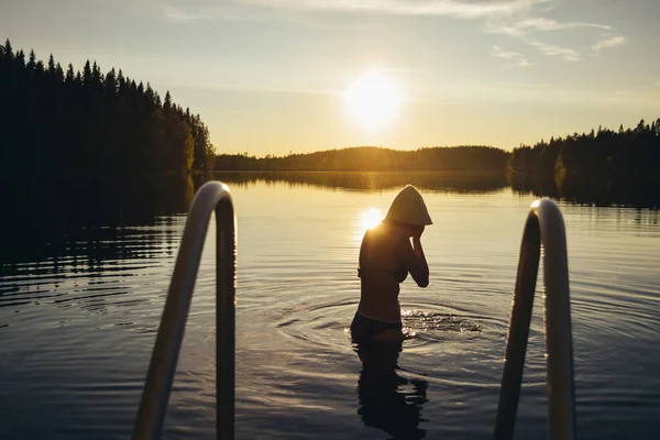 Finlandiya 'da saunadan sonra gün batımında gölde yüzen genç bir kadın.
