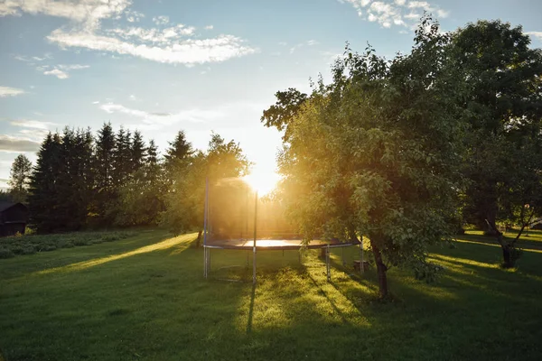 Trampolim de salto de crianças abertas ao sol em grama verde no quintal da casa de finlandês com árvores, noite de verão — Fotografia de Stock