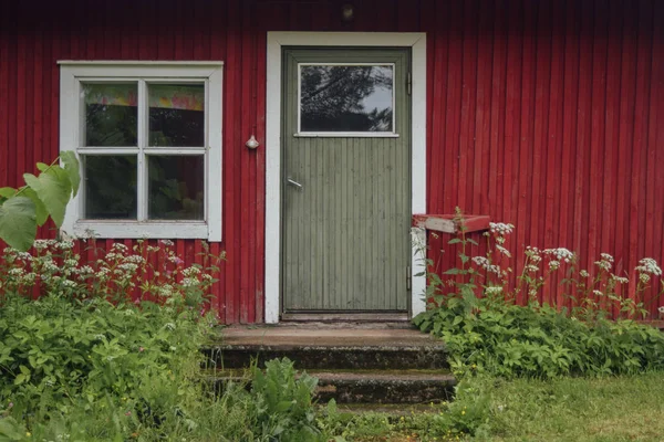 Entering to the red barn at finnish countryside strawberry farm, window and door with doorstep, summer misty day, green grass