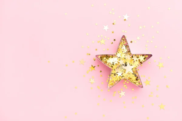 Pembe bayram havası. Kurabiye şeklindeki yıldız ve pastel pembe arka plandaki altın konfetiden yapılmış. Yaratıcı dekorasyon kavramı.