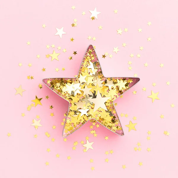 Pink festive flatly. Star made of cookie form and golden confetti at pastel pink background. Creative decoration concept.