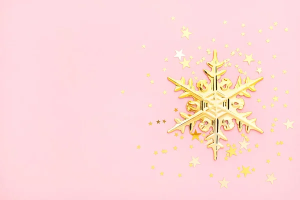 Pink christmas flatly. Golden snowflake and confetti at pastel pink background. New year layout with copyspace.