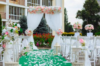 Güzel dekorasyon düğün töreni. Konuklar şenlikli Kemer yol açan çiçeklerle süslenmiş kaldırım tarafındaki beyaz Ahşap sandalyeler