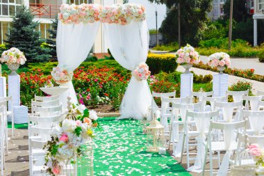 Güzel dekorasyon düğün töreni. Konuklar şenlikli Kemer yol açan çiçeklerle süslenmiş kaldırım tarafındaki beyaz Ahşap sandalyeler