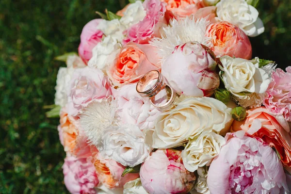 金の結婚指輪と緑の草の上に横たわる花の美しい花束 — ストック写真