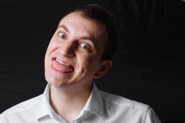 Ortodontik diş telleri beyaz görünüm, metal destekleri üzerinde dişlerini siyah bir zemin üzerine beyaz gömlekli bir adam portresi. Diş kavramı, tıbbi diş ortodontist hizalamasını