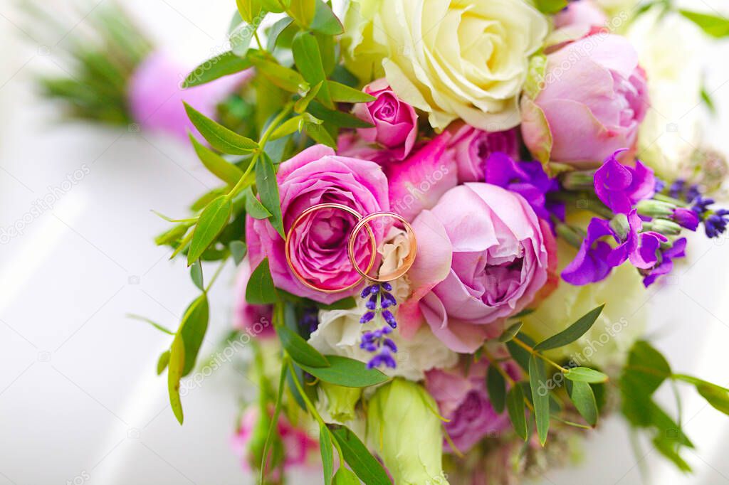 Close up of golden wedding rings of young and fresh flower bouquet of roses and other blooming beautiful flowers