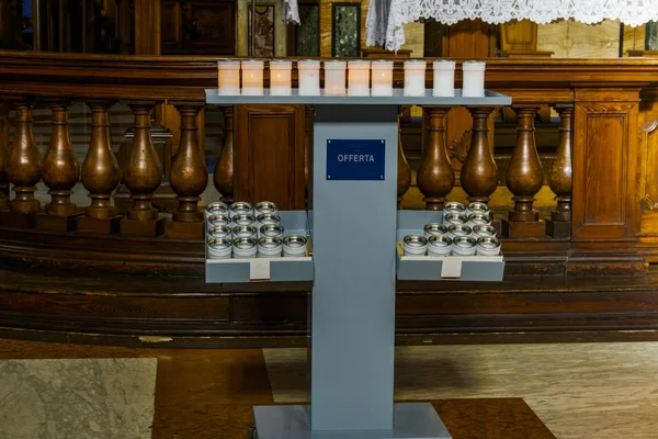 Prayer candles at a stand in a Catholic church. Lit and unlit white votive candles used for Christian prayer with an Italian offerta - offering sign.