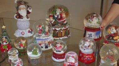 Birçok Noel kar küre topları bir tablo dekorasyon el. Noel Baba ve diğer mevsimlik figürleri tasvir şenlikli Noel kubbe topları koyarak kadın.