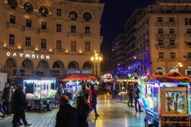 Thessaloniki, Yunanistan - 24 Aralık 2018: Aristotelous square, yerel Yunan sokak satıcıları. Işıklı römorklar pamuk şeker, kestane veya patlamış mısır satan etrafında Kalabalık cadde görünümü akşam.