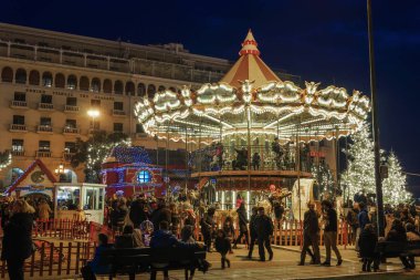 Thessaloniki, Greece - December 24 2018: Christmas 2018 decorations carousel at Aristotelous square. Evening view of unidentified crowd at Illuminated vintage fairground carousel with wooden horses. clipart