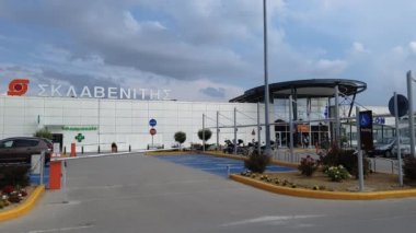 Thessaloniki, Yunanistan-Mayıs 14 2019: Sklavenitis süpermarket zincir girişi logosu ile. Yunan eczane işareti ve ışıklı yeşil haç ile alışveriş merkezi Makedonia, Hellenic Hipermarket Mağaza cephe