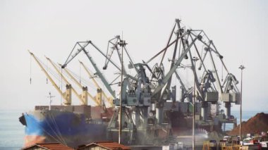Deniz limanında büyük motorlu vinçler gemilerden kargo boşaltma. Selanik Limanı'nın ticari rıhtım iskelesinde kargo taşıma gemi kıyı vinçler yükseltilmiş görünümü, Yunanistan.