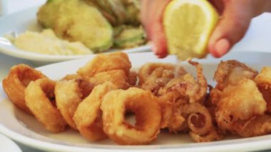 Yunan taverna restoranı kızarmış doğranmış kabak arka plan ile kalamar gıda closeup servis etti. Bir taverna masasında beyaz bir tabak üzerinde servis dilimler halinde gevrek kızarmış kalamar üzerine el serpme taze limon suyu.