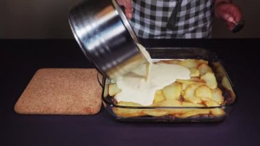 Yunan musakka yemeği tarifi hazırlama. Zeytinyağı, un, süt, yumurta, tuz ve karabiber ile beşamel beyaz sos ekleme ve kıyma üzerinde kızarmış doğranmış patates ile şeffaf kase.