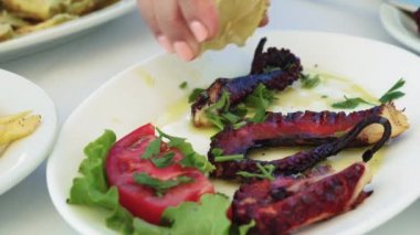 Yunan taverna restoranında ahtapot yakın çekim servis edilmektedir. Gevrek kömürleşmiş ahtapot dokunaçları üzerine el serpme taze limon suyu bir taverna masada beyaz bir tabak üzerinde servis.