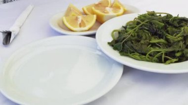 Tavern restoran gıda çatal ve kaşık yeşil beyazlatılmış sebze closeup ile hizmet vermektedir. Yunanistan'da bir taverna masada haşlanmış yapraklı yeşil salata-chorta ile beyaz çanak üzerine el taze limon suyu serpme taze limon suyu.