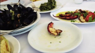 Taverna restoran Yunan meze deniz ürünleri çatal ve kaşık ile bir tabak üzerinde hizmet vermektedir. El servis ızgara ahtapot bacaklar, shell pişmiş midye ve taverna masada haşlanmış sebze ile kızarmış kabak cips.