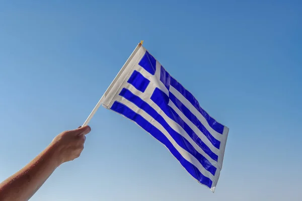 Hand waving Greek flag in the air for a national celebration. Blue & white Greek plastic flag with cross, celebrating the October 28 1940 Oxi Day against the Mussolini Italian 1940 ultimatum.