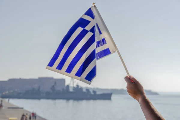 Hand waving Greek flag in the air for a national celebration.