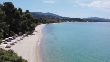 Akdeniz arazisi Yunan plaj insansız hava aracı görüntüsü. Sithonia Chalkidiki yarımadasının kumlu sahil kenarındaki yeşil plantasyonlu, kristal berrak deniz yatakları ve şemsiyeli deniz yatakları..