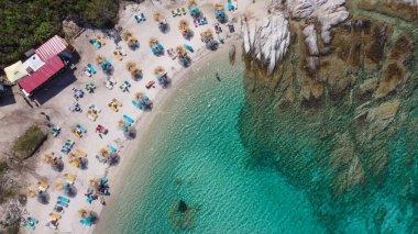 Akdeniz 'in insansız hava araçları Kavourotripes plajında yüzücülerle çekim yapıyor. Sithonia Chalkidiki yarımadası kayalık kıyı manzaralı, kristal berrak su yatakları ve şemsiyeli deniz yatakları.