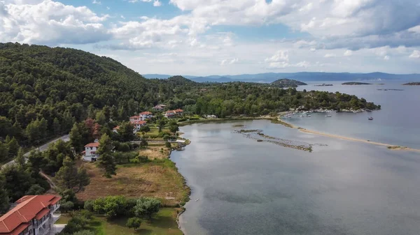 Mediterranean Greek landscape coastal drone shot. Aerial day top view of Sithonia Chalkidiki peninsula above shoreline with green plantation & low-rise houses by the sea.