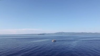 Yunanistan 'daki sakin denizde balıkçı teknesinin ardından insansız hava aracı uçuşu. Sithonia manzaralı Kassandra Chalkidiki yarımadasında Caique yelkenlisinin havadan görünüşü.