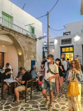 Milos, Yunanistan turistleri dar sokaklarda koruma maskeleri takıyorlar. Koronavirüslü insanlar akşam saatlerinde Cycladic Adası sokaklarında restoranın önünden geçerken korunuyorlar..