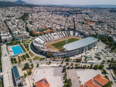 Thessaloniki, Greece landscape drone shot of PAOK FC Toumba stadium. Aerial top day view of empty football court with green pitch and team name written on the stands. clipart