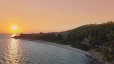 Akdeniz Yunan manzarasında turuncu gün batımı plaj dronu. Sithonia Chalkidiki yarımadasının gökyüzü manzarası kıyı üzerinde verimli yeşil tarlalar ve berrak sularla çevrili..