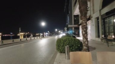 Selanik, Yunanistan 'da gece trafiği azaldı ve sahil kenarındaki kalabalık arttı. Nikis caddesinde hızla geçen araçlarla şehir yolunun yanında yürüyen kimliği belirsiz insanların aydınlık manzarası..
