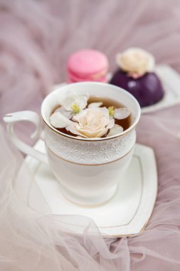 Hafif bir arka planda kompozisyon: çiçek yaprakları, tatlılar ve çiçeklerle çay. Çiçekler ve meyve çayıyla dolu bir hayat