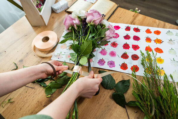 The florist's hands pack and decorate a bouquet of flowers. Packing pink roses in a bouquet in a flower shop.