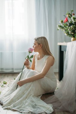 Gelinlik giymiş sarı saçlı güzel bir kız elinde bir gül tutuyor. Gelin, Apple ağaçlarıyla süslenmiş olarak stüdyoda fotoğraf çekimi yapıyor.