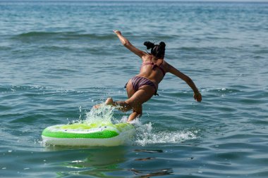 Genç kız plajda denizde şişme limonlu bir yatakta zıplıyor..