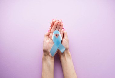 Kadının elindeki mavi kurdele pembe arka planda, düz bir zeminde. Dünya Diyabet Günü, 14 Kasım. 