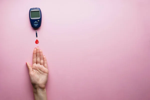 Diyabet konsepti. Dijital glukometre, bir damla kan ve pembe arka planda bir kadın eli. Dünya Diyabet Günü, 14 Kasım.