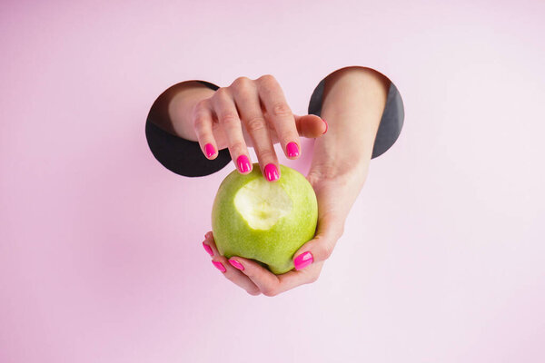 Beautiful manicure concept. Beautiful woman hands are holding an apple on a pink background. 