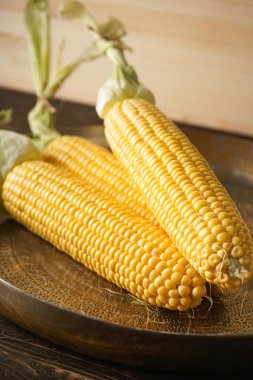 Bakır tepside olgun mısır ve ahşap arka planda bir havlu..
