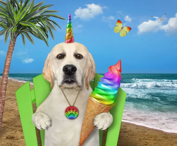 A dog unicorn eats a rainbow cone of ice cream under a palm tree on a beach chair on the seashore.