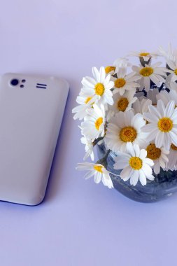 Papatyalar küçük bir buket yanında beyaz smartphone.