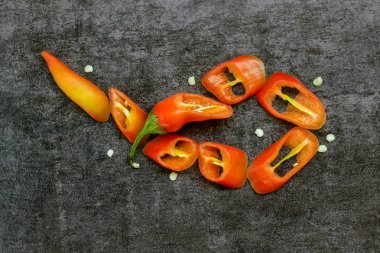 Parlak kırmızı ve turuncu biber karanlık taş zemin üzerine. Yüzük içine dilimlenmiş. Kavram - sıcak haber, baharatlar, yemek tarifleri, baharatlar. 