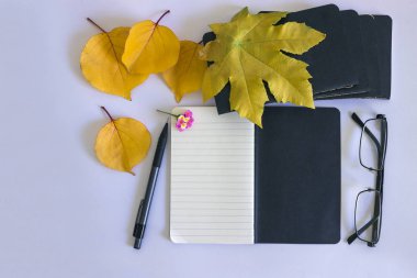 Notlar ve beyaz zemin üzerine sarı yapraklar için siyah not etmek. Kavram-sonbahar, yaratıcı ruh hali ve konfor.