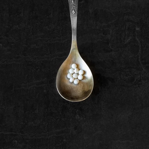 A lot of pills and  vitamins in a spoon on a dark background.  Concept- pharmacy, food additives, abuse and addiction to medicines drugs, drug addiction.