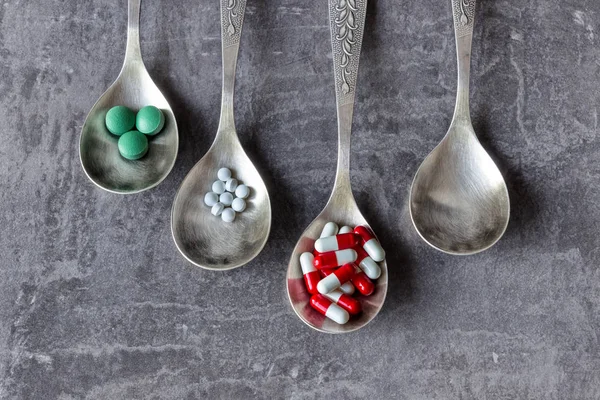 A lot of colored pills and medicines, vitamins, capsules in a spoon on a dark background.  Concept- pharmacy, food additives, abuse and addiction to medicines drugs, drug addiction.